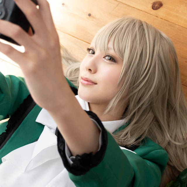 フローリングの床に寝ころび、一眼レフカメラで自撮りする女性の写真。