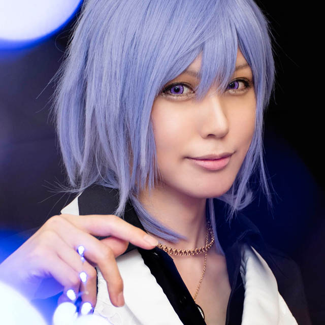 奥に立つ男装の女性にフォーカスすることで手前の電球がぼけ、光る球体が飛び交うように見える写真。