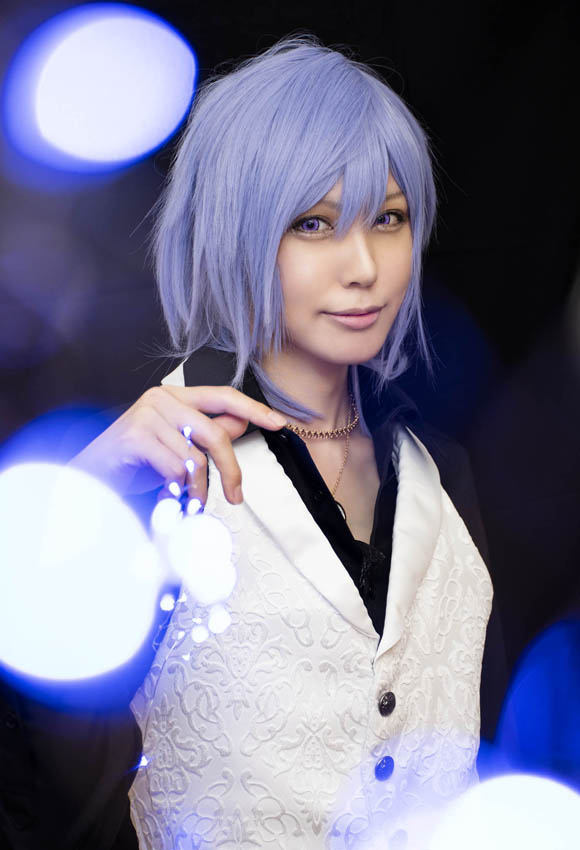 奥に立つ男装の女性にフォーカスすることで手前の電球がぼけ、光る球体が飛び交うように見える写真。