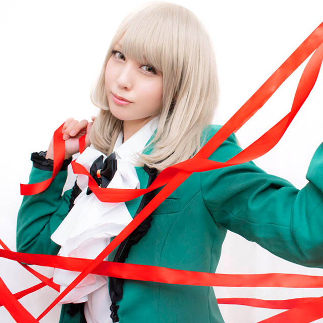 白い布を背景に、張り巡らされた赤いリボンの中に立つ女性の写真。