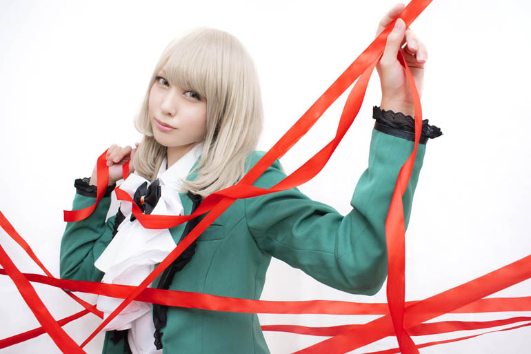 白い布を背景に、張り巡らされた赤いリボンの中に立つ女性の写真。