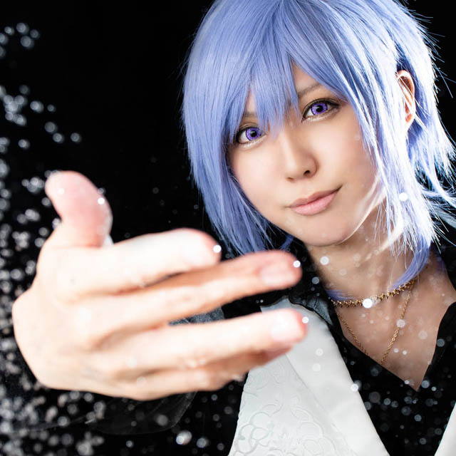 黒い布を背景に、こちらに向かって水しぶきを飛ばすように手を伸ばす男装の女性の写真。