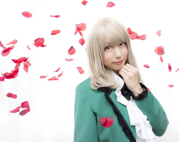 白い布を背景に、赤い花びらが舞う中に立つ女性の写真。