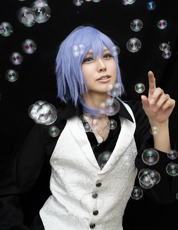 黒い布を背景に、シャボン玉の飛ぶ中に立つ男装の女性の写真。