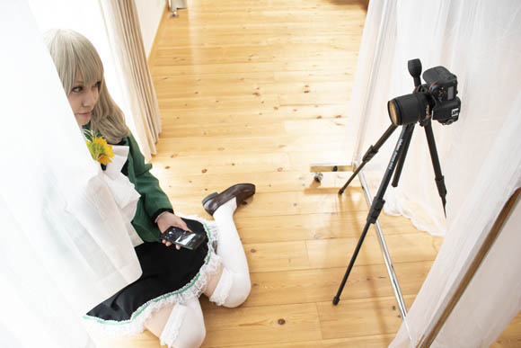 窓からの自然光を活かした、花を手に持って窓際に座る女性の写真の撮影風景。