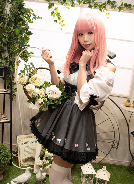 窓のそばに立ち、花かごを手にした女性の写真。