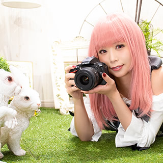 芝生の上で、兎のオブジェに一眼レフカメラを向ける女性の写真。