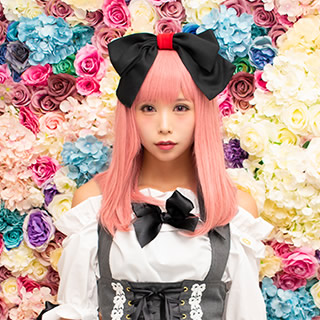 色とりどりの花を背景にした、大きなリボンをつけた女性の写真。