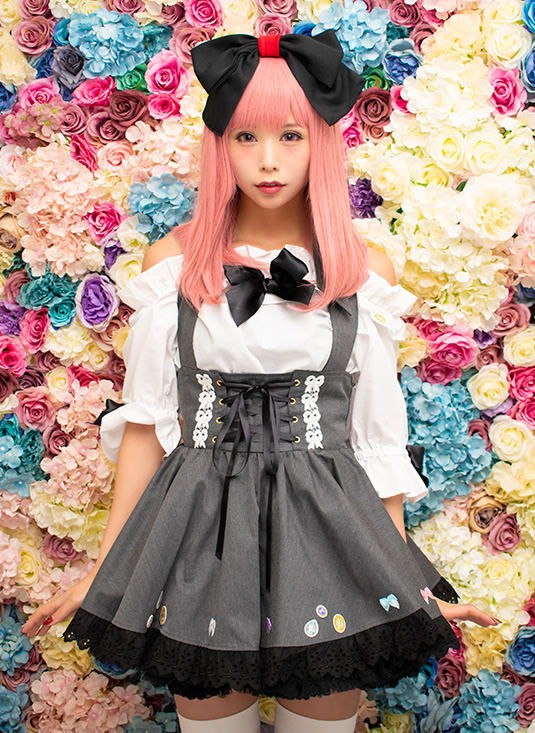 色とりどりの花を背景にした、大きなリボンをつけた女性の写真。