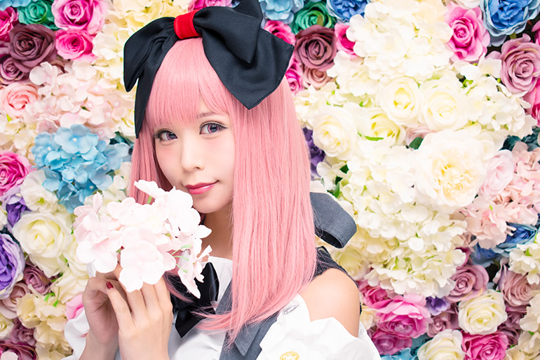 色とりどりの花を背景に、白い花を持って微笑む女性の写真。