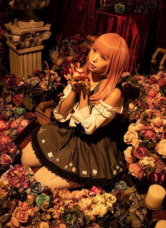 アンティーク調の部屋の中で、薔薇を手にして座り込む女性の写真。