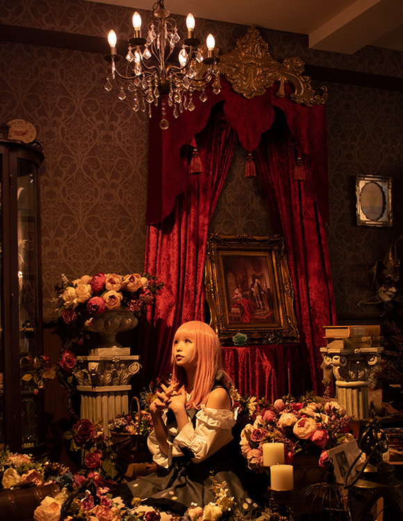 アンティーク調の部屋の中で、シャンデリアの下に座り込む女性の写真。