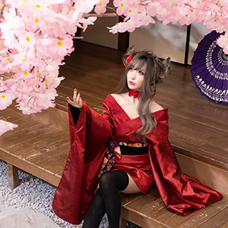 縁台に腰掛け、庭の桜を見上げる赤い着物の女性の写真。