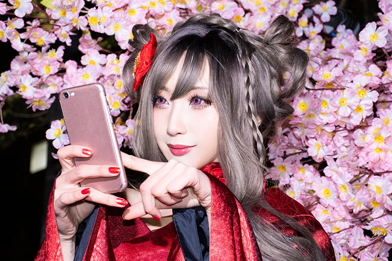 桜を背景に、撮影した写真をスマホで確認する赤い着物の女性の写真。