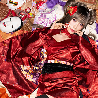 部屋中に広げた着物や帯の上に寝転び、花札を1枚手にした赤い着物の女性の写真。