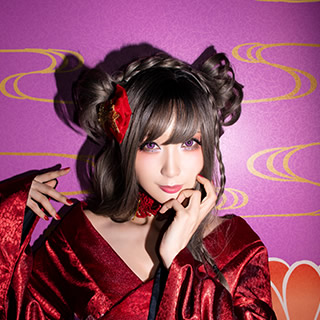 紫色の襖を背にしてこちらを見つめる赤い着物の女性の写真。