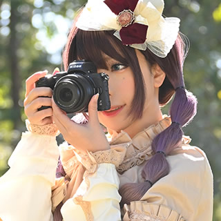 切り株に腰掛け、カメラのシャッターを切る女性の写真。