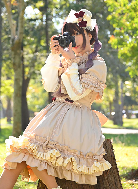 切り株に腰掛け、カメラのシャッターを切る女性の写真。