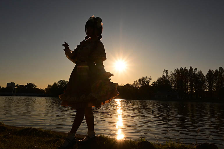 夕景バックに川沿いに佇む女性のシルエット写真。