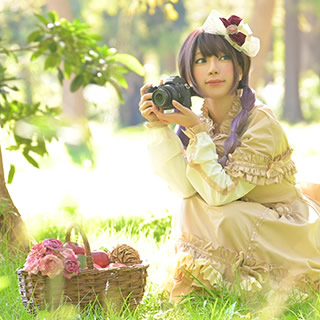 木立の中でしゃがんでカメラを持ち微笑む女性の写真