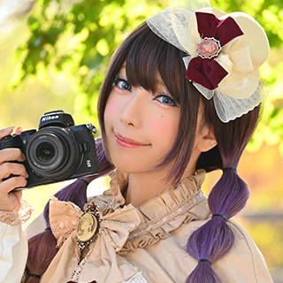 木立の下でカメラを持ち、にっこりほほ笑む女性の写真