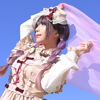 青空の下、ヴェールを持って風を感じる女性の写真。