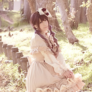 小川沿いのフェンスに腰掛けこちらを見つめる女性の写真。