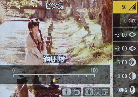 小川沿いのフェンスに腰掛けこちらを見つめる女性の液晶画面の写真。